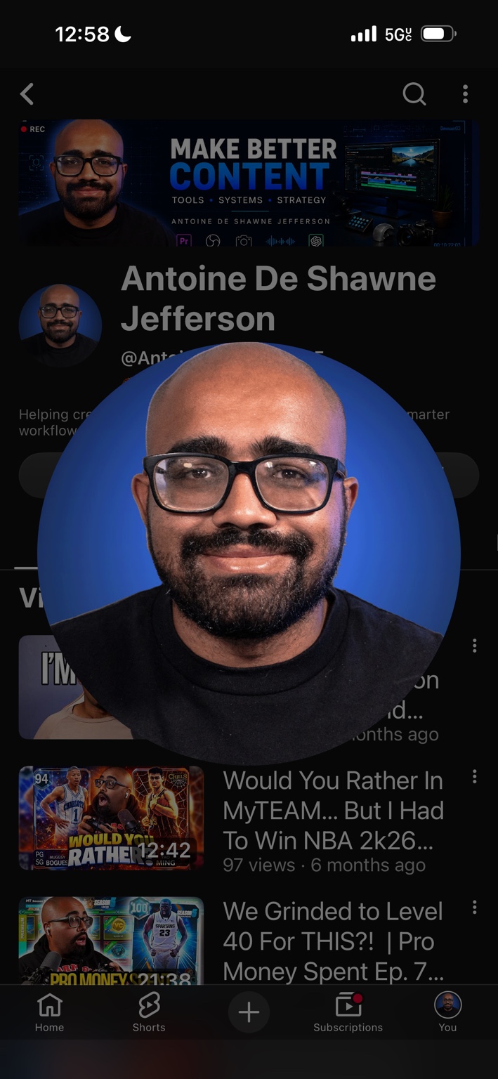 Antoine De Shawne Jefferson smiling, wearing glasses and a black shirt against a blue background
